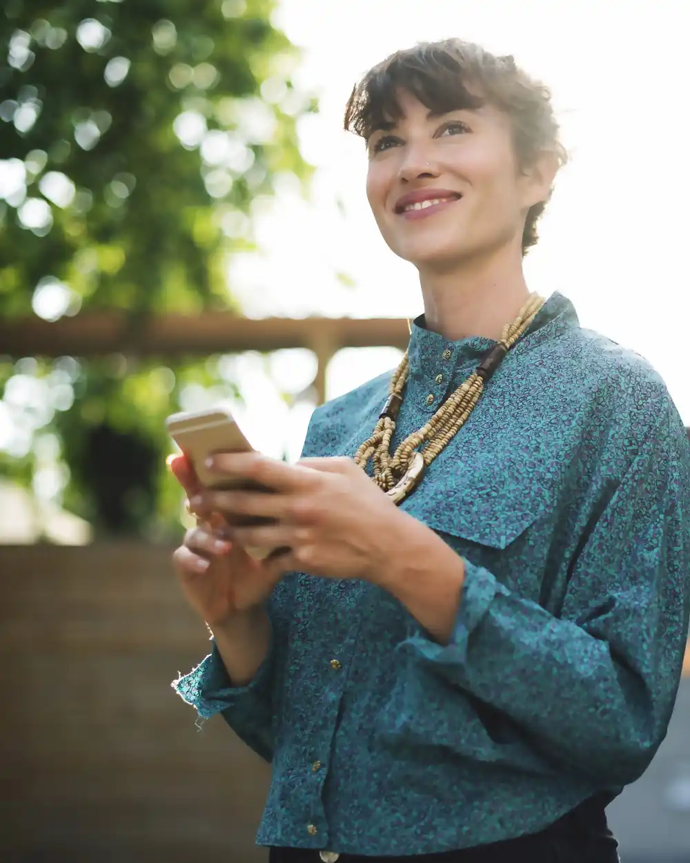 A woman smiling as she reads a message on her phone outdoors